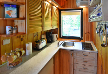 Compacte houten lodgekeuken met raam, kastjes, koffiezetapparaat, broodrooster en keukengerei op rij.