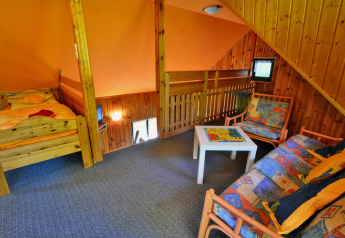 Knus zoldergedeelte van een lodge met een eenpersoonsbed, bank, salontafel en houten bekleding.