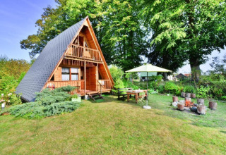 A-vorm zomerhuis met tuin, terras, parasol en vuurplaats in een groene omgeving in Denemarken.