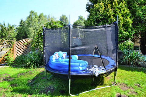 Trampolin med sikkerhedsnet og en blå oppustelig børnepool, set i en have ved feriebolig i Kołobrzeg.