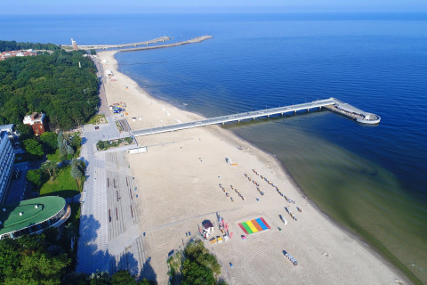 Vista aerea di una spiaggia sabbiosa e molo lungo la costa di Kołobrzeg, Polonia, con aree verdi circostanti.