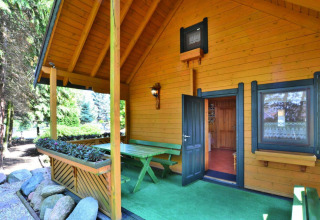Træhytte med overdækket terrasse, grønne omgivelser og udendørs siddeområde i Kołobrzeg, Danmark.