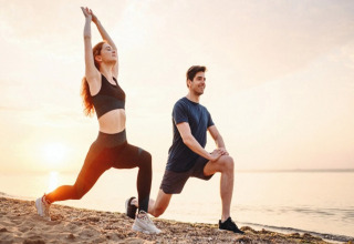 Twee mensen doen rekoefeningen op het strand bij zonsondergang, gekleed in sportkleding en ontspannen.
