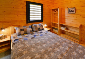 Acogedor dormitorio en alojamiento glamping con paredes de madera, cama doble y estantes abiertos.
