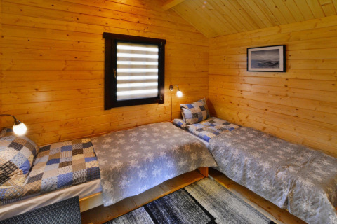 Træbeklædt glampingværelse med to enkeltsenge, moderne sengetøj, væglamper og et vindue.