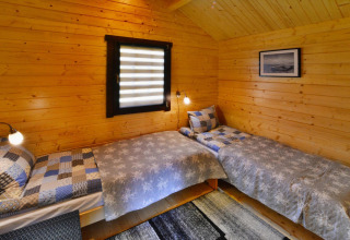 Træbeklædt glampingværelse med to enkeltsenge, moderne sengetøj, væglamper og et vindue.