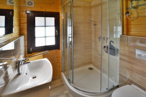 Moderne badeværelse i glamping-indkvartering med brusekabine, håndvask og træpanelvægge.