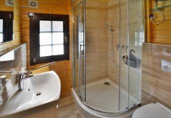 Baño moderno en alojamiento glamping con ducha redondeada, lavabo, espejo y paredes de madera.