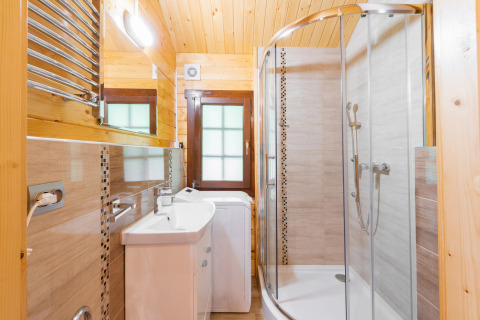 Bright bathroom at a glamping accommodation featuring a shower, sink, washing machine, and wooden walls.