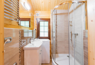 Bright bathroom at a glamping accommodation featuring a shower, sink, washing machine, and wooden walls.