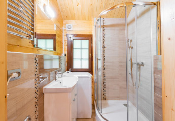 Baño luminoso en alojamiento glamping con cabina de ducha, lavamanos, lavadora y paredes de madera.