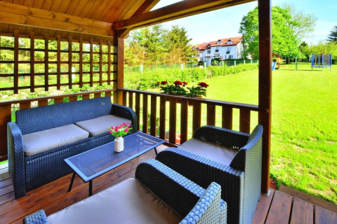 Udendørs opholdsområde på glamping med kurvemøbler under trætag, med udsigt til grøn plæne og villa.