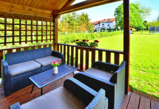 Udendørs opholdsområde på glamping med kurvemøbler under trætag, med udsigt til grøn plæne og villa.