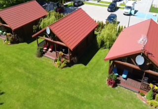 Three cozy cabins with red roofs and porches on a lush green lawn at a modern glamping accommodation.