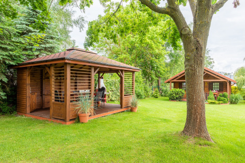 To hyggelige træhytter står på en grøn græsplæne omgivet af træer, velegnet til glamping.
