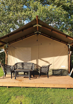 Tienda safari con terraza de madera y muebles exteriores en Camping de Oude Rijn, Países Bajos, rodeada de árboles.