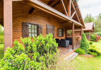 Acogedora cabaña de madera tipo glamping con porche cubierto, muebles al aire libre y jardín verde.