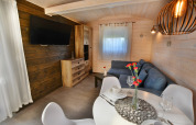 Acogedora sala de estar en cabaña moderna con sofá azul, mesa de comedor, televisor y luz natural.