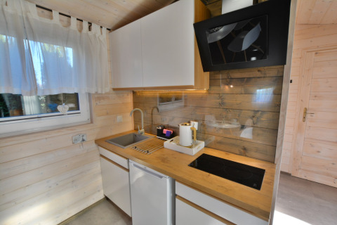 Moderne keuken in houten huisje met witte kasten, spoelbak, kookplaat en raam in Ustronie Morskie.