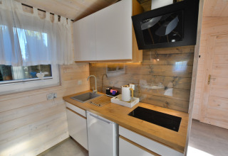 Moderne keuken in houten huisje met witte kasten, spoelbak, kookplaat en raam in Ustronie Morskie.