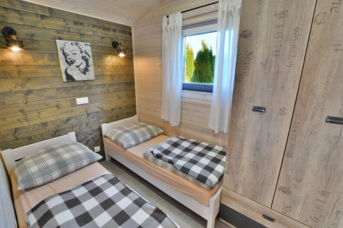 Slaapkamer in een moderne houten blokhut met twee eenpersoonsbedden, kast, raam en geruite decoratie.