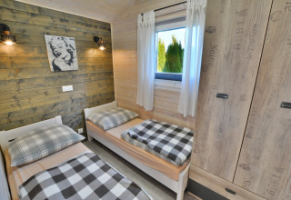 Slaapkamer in een moderne houten blokhut met twee eenpersoonsbedden, kast, raam en geruite decoratie.