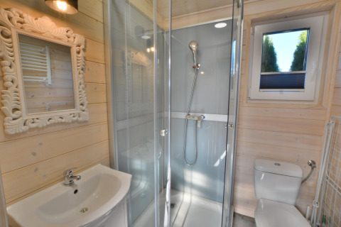 Baño moderno en cabaña de madera con ducha acristalada, espejo decorativo, lavabo y ventana en Ustronie Morskie.