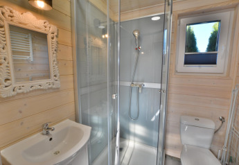 Modern bathroom in a wooden cabin featuring a glass shower, ornate mirror, small window, sink, and toilet.