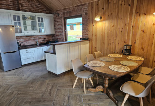 Cozy lodge kitchen with wooden walls, dining table for six, modern fridge, and a coffee maker on the table.