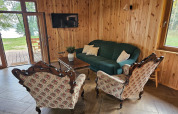 Salon d’un lodge aux murs en bois, canapé vert, fauteuils à motifs floraux, TV et vue sur le jardin.