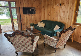 Sala de estar de una cabaña con paredes de madera, sofá verde, sillones florales y televisor de pared.
