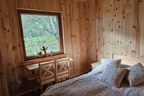 Slaapkamer in een houten lodge met ruim raam, gezellige bed en twee stoelen aan het bureau.