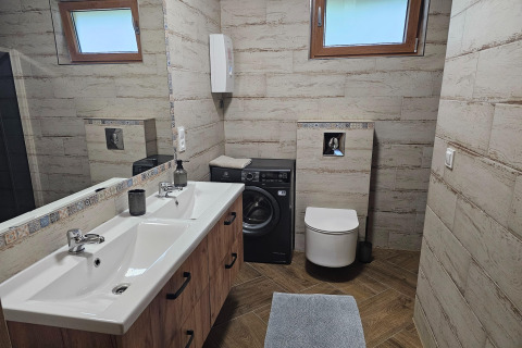 Moderne badeværelse med dobbelthåndvask, vaskemaskine under hylde, toilet og store vinduer i en lodge.