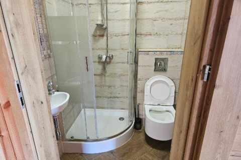 Kleine lodge-badkamer met douchecabine, toilet en wastafel. Houten deur zichtbaar op de voorgrond.