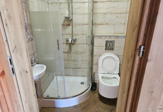 Kleine lodge-badkamer met douchecabine, toilet en wastafel. Houten deur zichtbaar op de voorgrond.