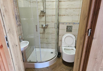 Kleine lodge-badkamer met douchecabine, toilet en wastafel. Houten deur zichtbaar op de voorgrond.