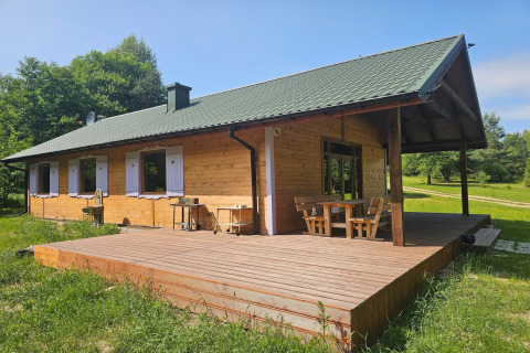 Wooden lodge with spacious porch set in lush greenery, perfect for relaxing on a bright sunny day.