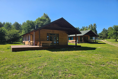 Wooden cabins on a grassy clearing at a lodge, surrounded by green trees under a bright blue sky.