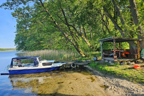 Foto di una piccola barca al molo e di una tettoia in legno sulla riva del lago circondata da alberi.