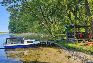 Picture of a small boat at a dock and a covered wooden hut by the lake shore surrounded by trees.