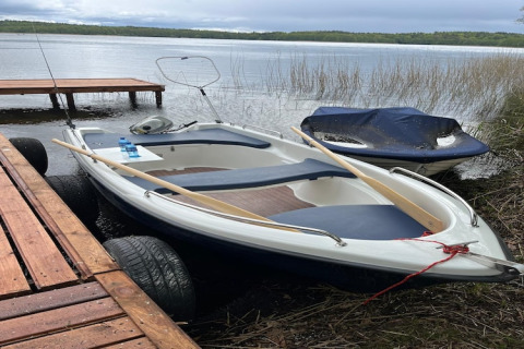 Roeiboot met roeispanen en fles water aangemeerd bij een houten steiger bij een lodge aan het meer.