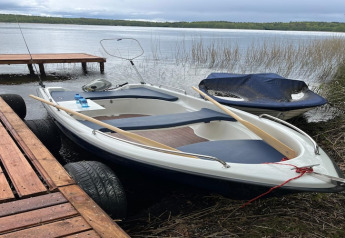 Barque avec rames et bouteille d’eau amarrée à un ponton en bois près d’un lodge au bord d’un lac.