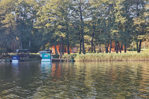 Foto di un tranquillo lodge sul lago con barche ormeggiate e alberi illuminati dalla luce solare.