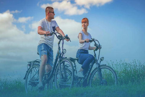 Een jong stel maakt een fietstocht op een groene weide bij hun glampingaccommodatie onder een blauwe lucht.