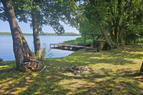 Lakeside view with pier, fire pit, and woodpile at LAWENDA holiday cottage in Grąbczyn, Denmark.