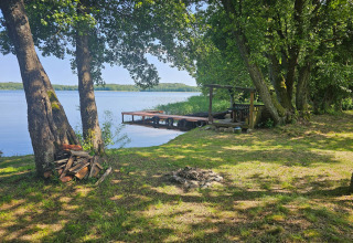 Boomrijke oever, steiger, vuurplaats en houtstapel bij LAWENDA vakantiehuis in Grąbczyn, Denemarken.