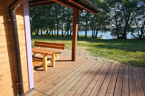 Terras van LAWENDA vakantiehuis in Grąbczyn met houten banken en uitzicht op het meer en bomen.