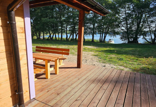 Deck at LAWENDA holiday cottage in Grąbczyn featuring wooden benches and lake view with trees and boat.