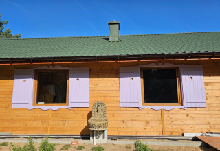 Holiday cottage with green roof, lavender shutters and outdoor fountain beneath blue sky in Grąbczyn, Denmark.