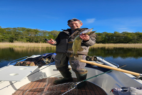 Man fishing on a boat at LAWENDA holiday cottage in Grąbczyn, Denmark, proudly holds up a caught fish.